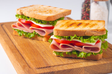 Close-up of two sandwiches with bacon, salami, prosciutto and fresh vegetables on rustic wooden cutting board. Club sandwich concept