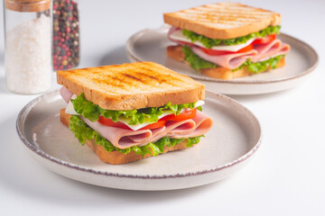 Close-up of two sandwiches with bacon, salami, prosciutto and fresh vegetables on rustic wooden cutting board. Club sandwich concept