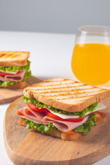 Close-up of two sandwiches with bacon, salami, prosciutto and fresh vegetables on rustic wooden cutting board. Club sandwich concept