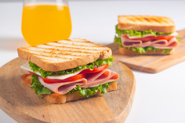 Close-up of two sandwiches with bacon, salami, prosciutto and fresh vegetables on rustic wooden cutting board. Club sandwich concept