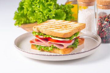 Close-up of two sandwiches with bacon, salami, prosciutto and fresh vegetables on rustic wooden cutting board. Club sandwich concept