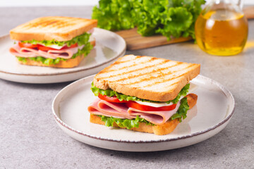 Close-up of two sandwiches with bacon, salami, prosciutto and fresh vegetables on rustic wooden cutting board. Club sandwich concept