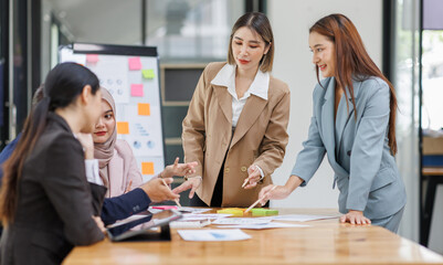 Group of asian professionals collaborating and working together in a  office. They are discussing project solutions and working on paperwork. The team looks happy, successful.
