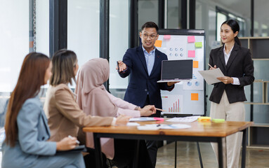 Group of asian professionals collaborating and working together in a  office. They are discussing project solutions and working on paperwork. The team looks happy, successful.
