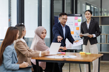 Group of asian professionals collaborating and working together in a  office. They are discussing project solutions and working on paperwork. The team looks happy, successful.
