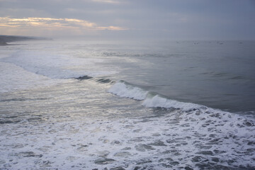 Panoramic View of Wide Coastline at Sunset, Gentle Waves, Overcast Sky with Sun Rays, Serene Coastal Landscape in High Resolution