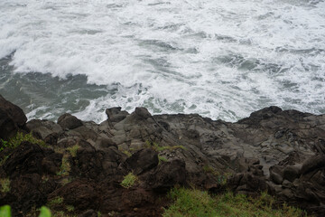 Close-Up View of Rocky Shore with Crashing Ocean Waves, Rugged Coastal Landscape, Natural Texture of Rocks and Sea Foam