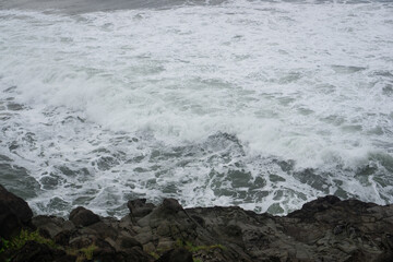 Close-Up View of Rocky Shore with Crashing Ocean Waves, Rugged Coastal Landscape, Natural Texture of Rocks and Sea Foam