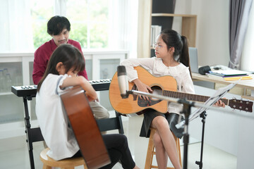 children concentrate on playing guitar with teacher in the classroom,adult help kid to learn music,concept of music studying,music education,art class,classical band