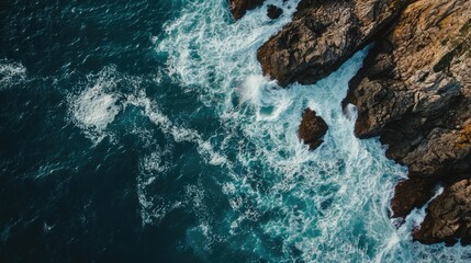 Obraz premium Aerial view of ocean waves crashing against rocky shoreline with clear space for text or branding placement