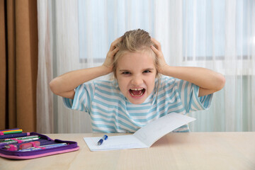 sad tired girl of eight holds her head in her hands and screams does homework sitting at the table at home