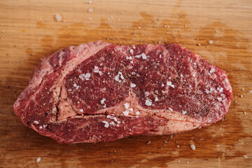 Raw ribeye steak spiced and ready to cook on oak board