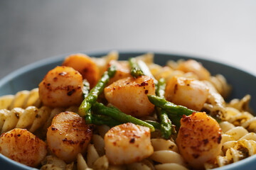 Fusilli pasta with scallops and asparagus in blue bowl closeup