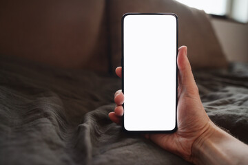 man hand holding phone with white screen over bed on background