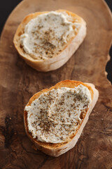Ciabatta slices with cream cheese and herbs on olive wood board