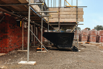 Construction site with scaffolding and dumpster skip during daylight hours