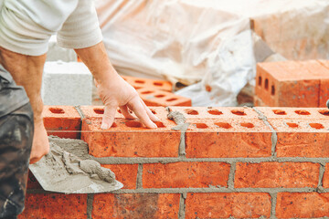 close-up of Bricklayer working on a wall construction project using clay bricks and mortar in a residential area