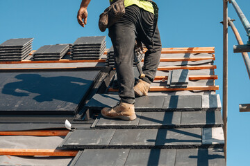 Skilled roofer installing slate tiles on a building under clear blue sky