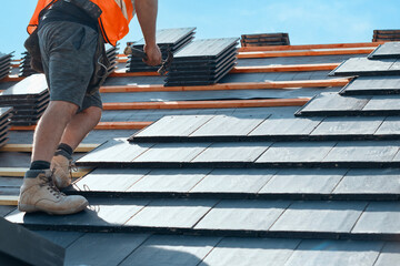 Roofing project in progress with worker installing slate tiles on a sunny day