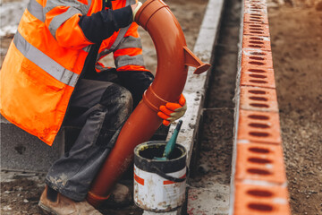 Construction worker installing plastic drainage pipe at a building site in early morning light