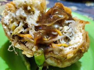 Tahu Isi or Tahu Brontak is an Indonesian food made from fried tofu with several types of vegetables including cabbage, mustard greens, bean sprouts and carrots. Served with chili on a green plate.