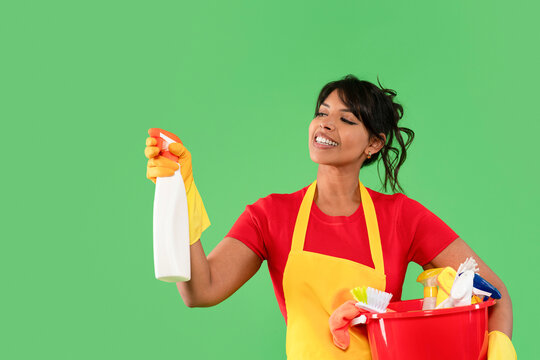 Happy woman cleaning with spray bottle and bucket in a bright green setting