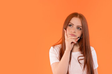 Thoughtful woman with long red hair contemplating against an orange background