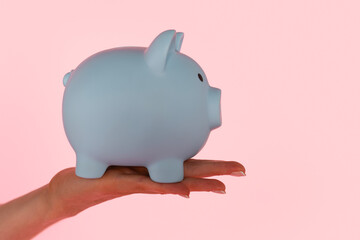 Hand holding a blue piggy bank against a pink background during a savings theme