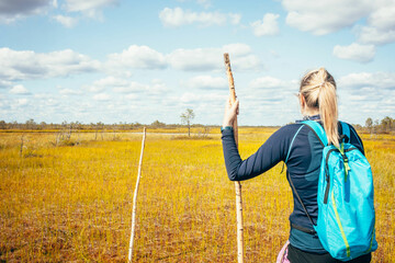 A hiker explores the vast landscape of the Vasyugan Mire with a backpack and walking stick. The golden wetland grasses and blue sky provide a striking backdrop, emphasizing the scale and remoteness of