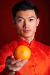 Asian Man in Red Traditional Attire Holding an Orange