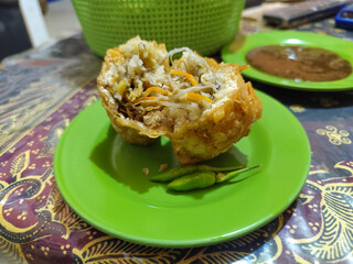 Tahu Isi or Tahu Brontak is an Indonesian food made from fried tofu with several types of vegetables including cabbage, mustard greens, bean sprouts and carrots. Served with chili on a green plate.