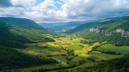 Fototapeta premium Expansive mountain valley, lush green meadows, dramatic cloudy sky, sunlit patches, aerial perspective, rolling hills, distant mountains, serene landscape, vibrant colors, natural beauty