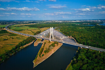 Cable stayed bridge over river surrounded by lush green forest. Redzinski bridge over Odra river with cars driving on highway in Wroclaw, Poland