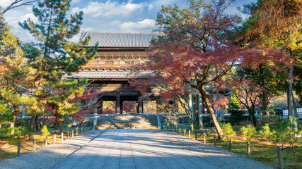 A stone path lined with vibrant autumn foliage leads to the grand wooden gate of Nanzen-ji Temple....