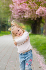 Obraz premium Little blonde girl smiling against the background of blooming trees in spring