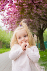 portrait of a cute little blonde girl against the background of blooming trees in spring