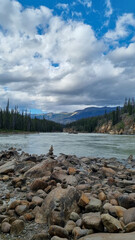 View over Athabasca River flowing from nearby Athabasca Falls, Jasper National Park, AB, Canada, with white-water raft in distance on river and river shore with colorful rock formations of limestone