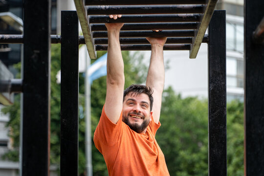 Hombre sonriente entrenando haciendo balanceos en barras. Entrenamiento al aire libre en parque p&uacute;blico