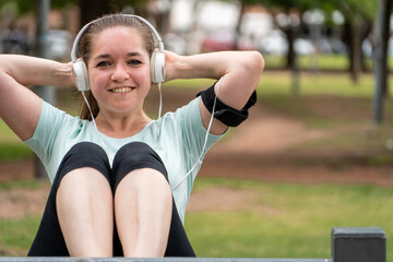 Mujer sonriente entrenando en el parque, haciendo abdominales mientras escucha música