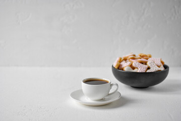 A white cup of coffee and a black bowl of heart-shaped cookies with pink icing. White background, empty space for text.