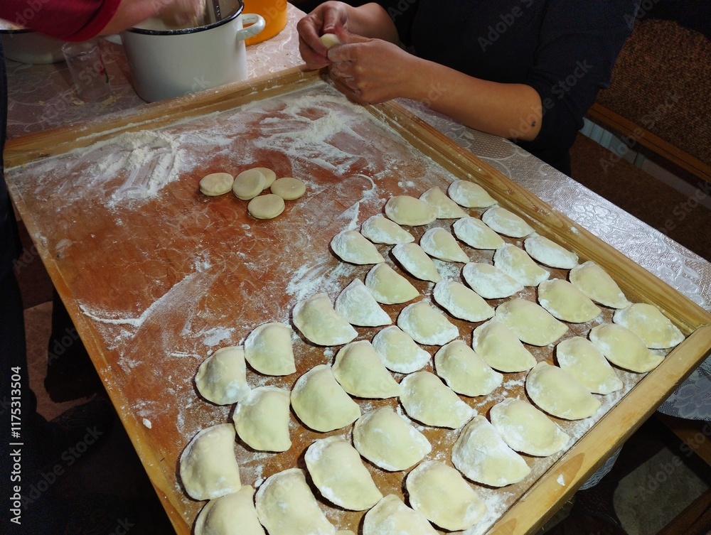 Wall mural Woman manually makes varenyki. In the photo, female hands are molding varenyki. Raw varenyki are laid out on a wooden board. Cooking theme.