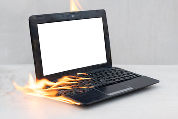 An open black laptop with a white mock up on the screen burning on fire on a gray background close-up