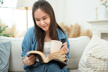 Young Asian woman enjoying reading book in living room at home