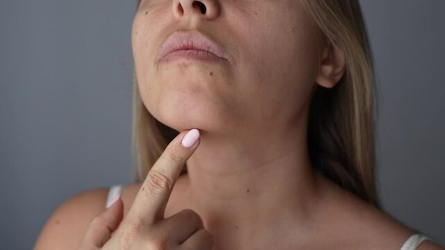 Close up of young caucasian blonde woman touching her chin with dimple on it with her finger on a dark grey background. Mentoplasty concept