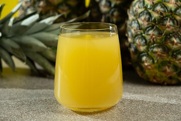 Pineapple juice in a glass among fresh pineapple fruit close-up.