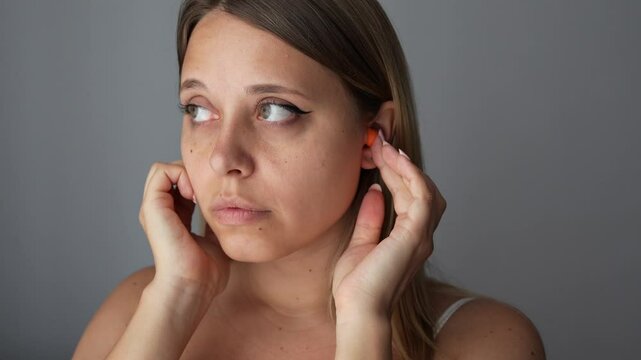 Close up of a young woman putting polyurethane earplugs in her ears with her hands on a dark gray background. Anti-noise earbuds for sleep, rest, travel, airplane