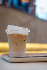 A glass of iced latte with milk in a clear plastic cup on a white wooden tray