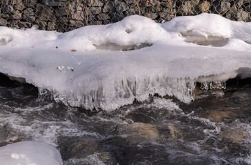a rocky mountain river with a bank covered with snow and ice