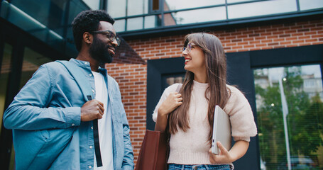 Multi-ethnic coworkers getting to know each other closer after work. Friends having small talk before going home. Giving high five. Laughing and smiling before saying goodbye. Working in office.
