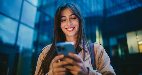 Evening in city. Cute Caucasian girl finishing entering text on her smartphone. Lowering mobile...